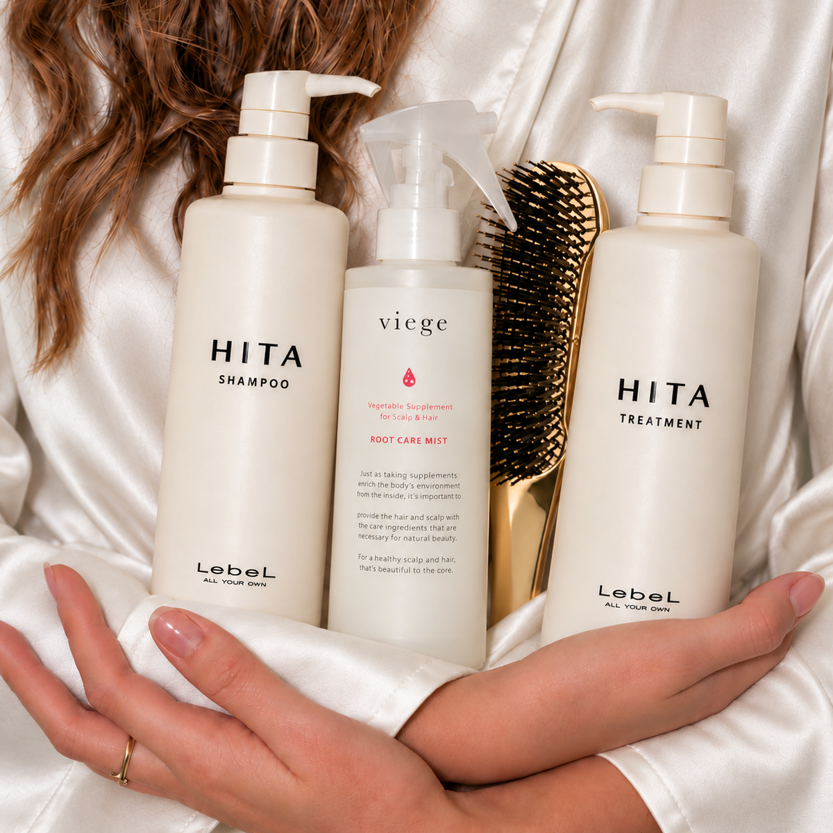 Kobieta w białym szlafroku trzyma kosmetyki LebeL HITA, Viege Root Care Mist i złotą szczotkę do włosów.